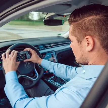 Mann sitzt im Auto und bedient ein Navigationsgerät am Steuer.