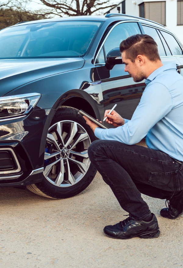 Ein Mann überprüft das Rad eines schwarzen Autos und macht Notizen.